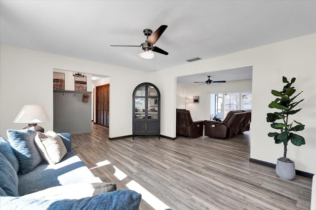 living room with light wood-style floors, visible vents, baseboards, and a ceiling fan