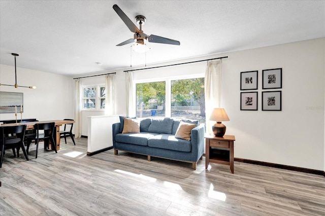 living room featuring a ceiling fan, light wood-type flooring, a textured ceiling, and baseboards