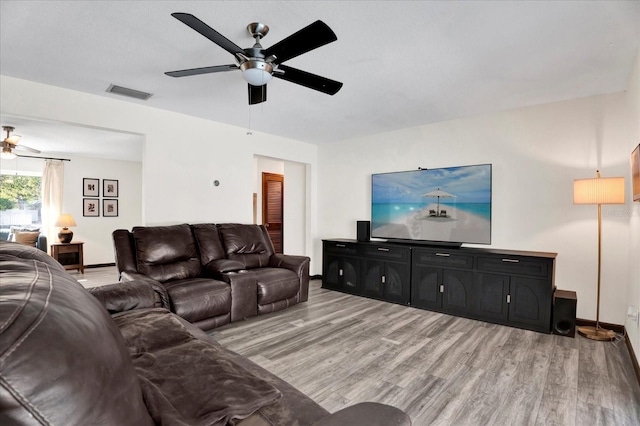 living room featuring light wood finished floors, baseboards, visible vents, and ceiling fan