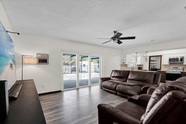 living area featuring a ceiling fan, a textured ceiling, baseboards, and wood finished floors