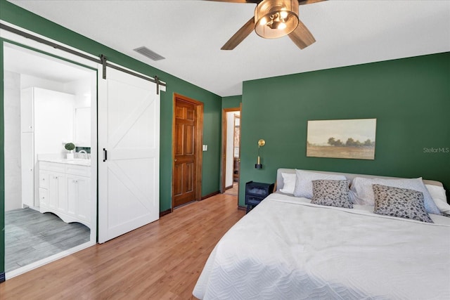 bedroom featuring visible vents, a barn door, light wood-style floors, a ceiling fan, and a sink