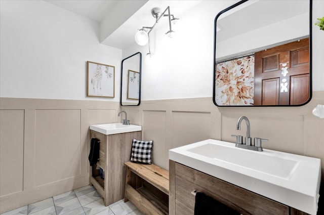 full bath with two vanities, a wainscoted wall, a sink, and a decorative wall