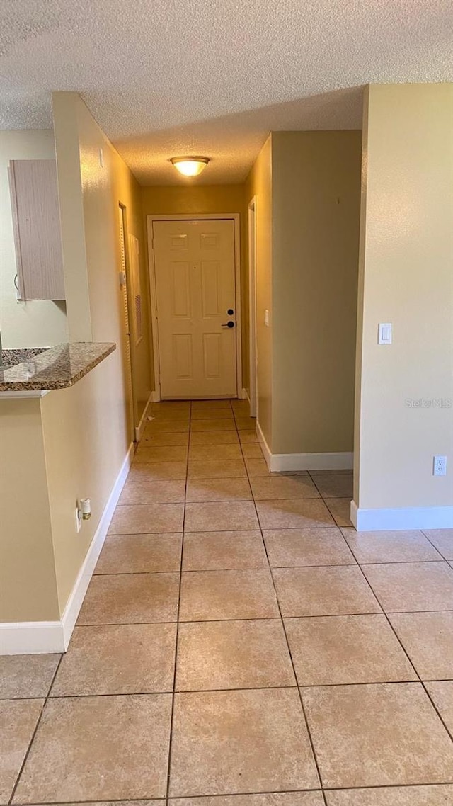 hallway with a textured ceiling, baseboards, and light tile patterned floors