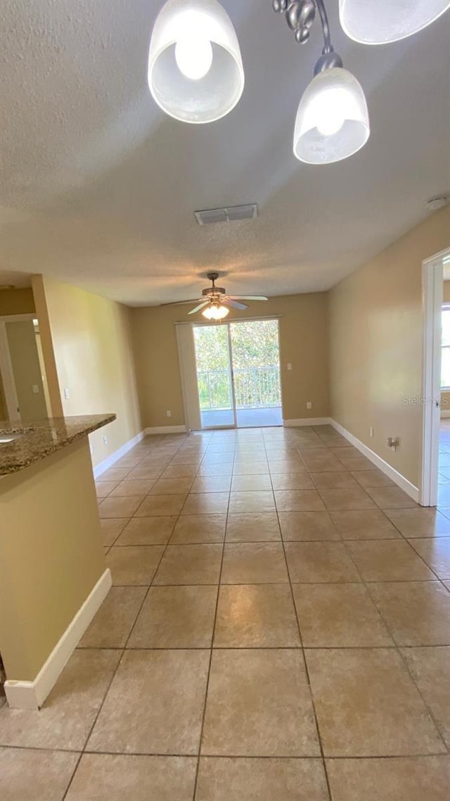 empty room featuring light tile patterned floors, ceiling fan, baseboards, and a textured ceiling