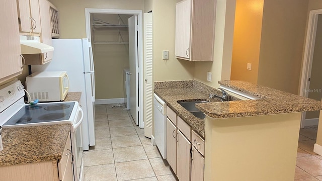 kitchen with stone countertops, a sink, white appliances, a peninsula, and under cabinet range hood