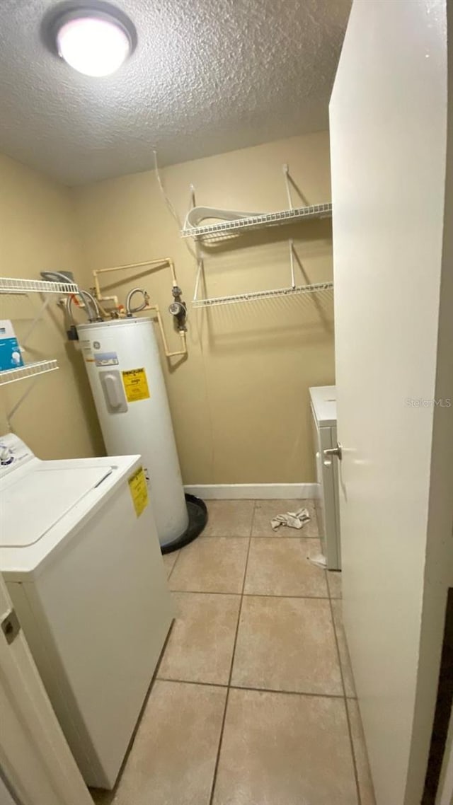 laundry area with electric water heater, light tile patterned flooring, a textured ceiling, washer / dryer, and laundry area