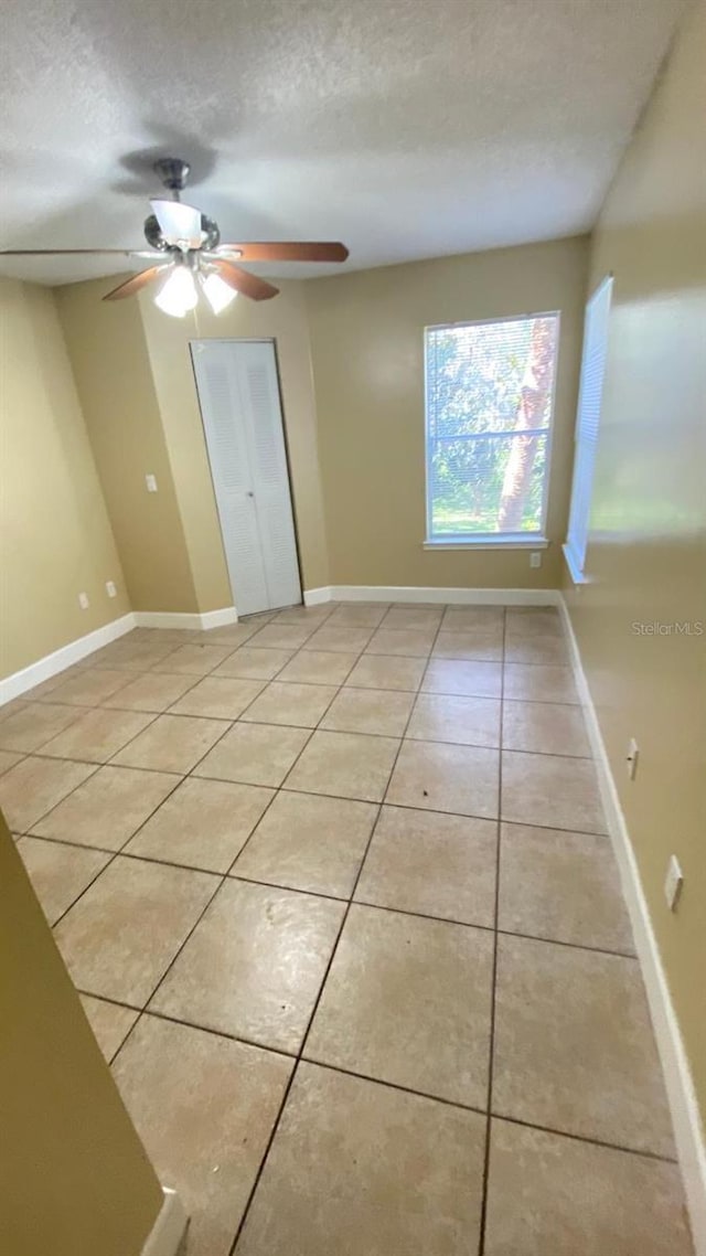 unfurnished room with a textured ceiling, ceiling fan, light tile patterned floors, and baseboards