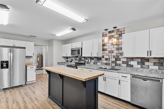 kitchen featuring butcher block countertops, appliances with stainless steel finishes, hanging light fixtures, white cabinetry, and a sink