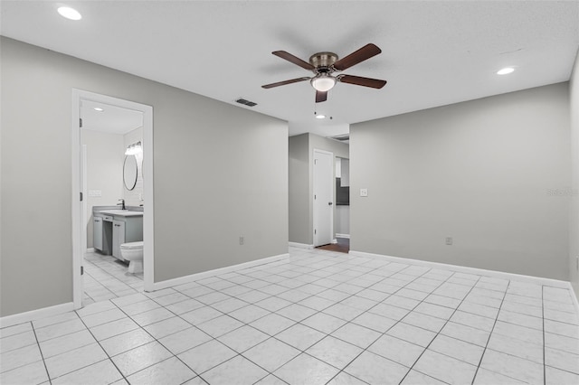 empty room featuring ceiling fan, light tile patterned flooring, a sink, visible vents, and baseboards