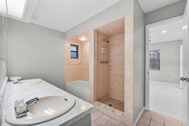 bathroom featuring double vanity, tile patterned flooring, a tile shower, and a sink