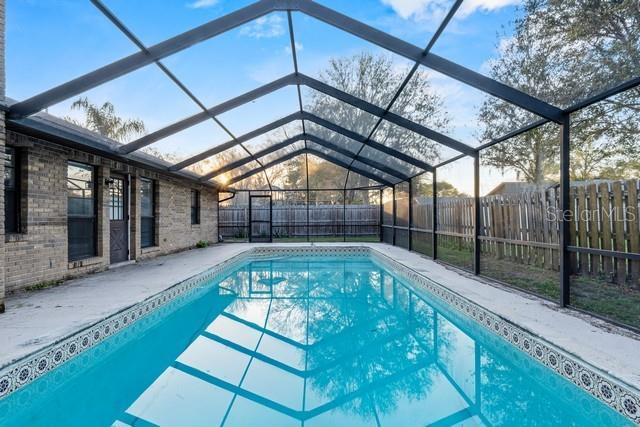 view of swimming pool featuring glass enclosure, a patio, a fenced backyard, and a fenced in pool