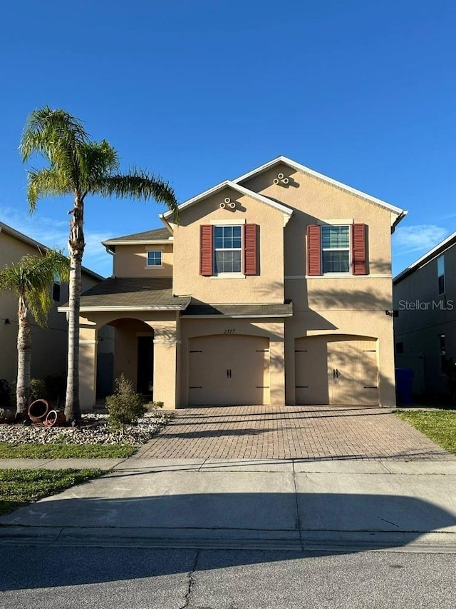 traditional-style home with an attached garage, decorative driveway, and stucco siding