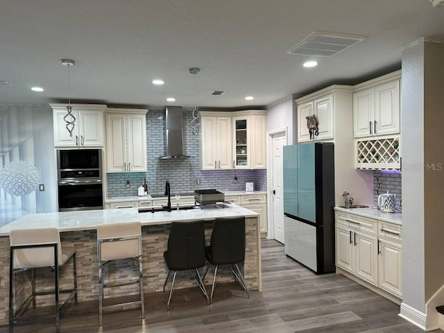 kitchen featuring light countertops, visible vents, freestanding refrigerator, a sink, and wall chimney exhaust hood