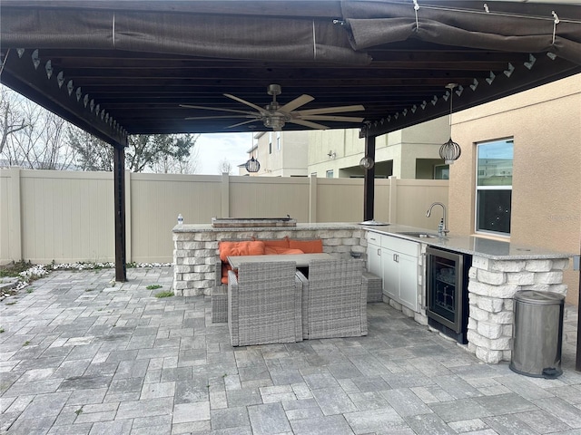 view of patio / terrace featuring beverage cooler, an outdoor kitchen, ceiling fan, fence, and a sink