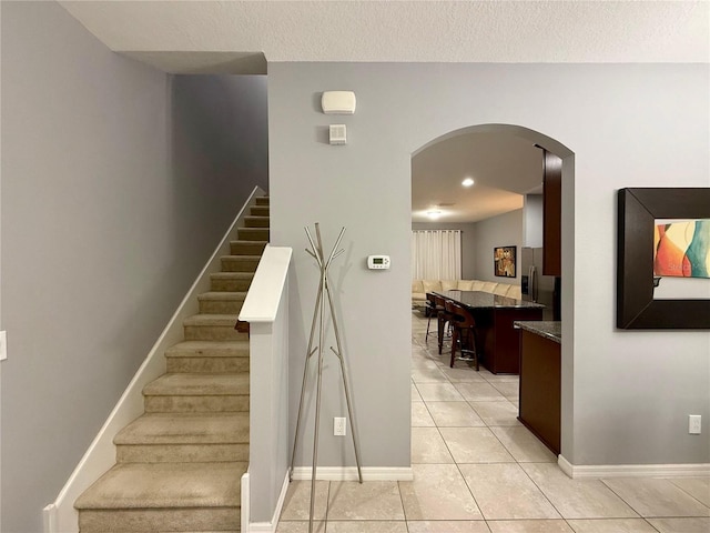 staircase with baseboards, tile patterned flooring, arched walkways, and a textured ceiling