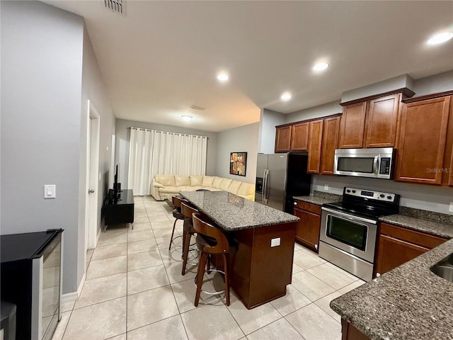 kitchen with light tile patterned floors, stainless steel appliances, a kitchen island, visible vents, and a kitchen breakfast bar