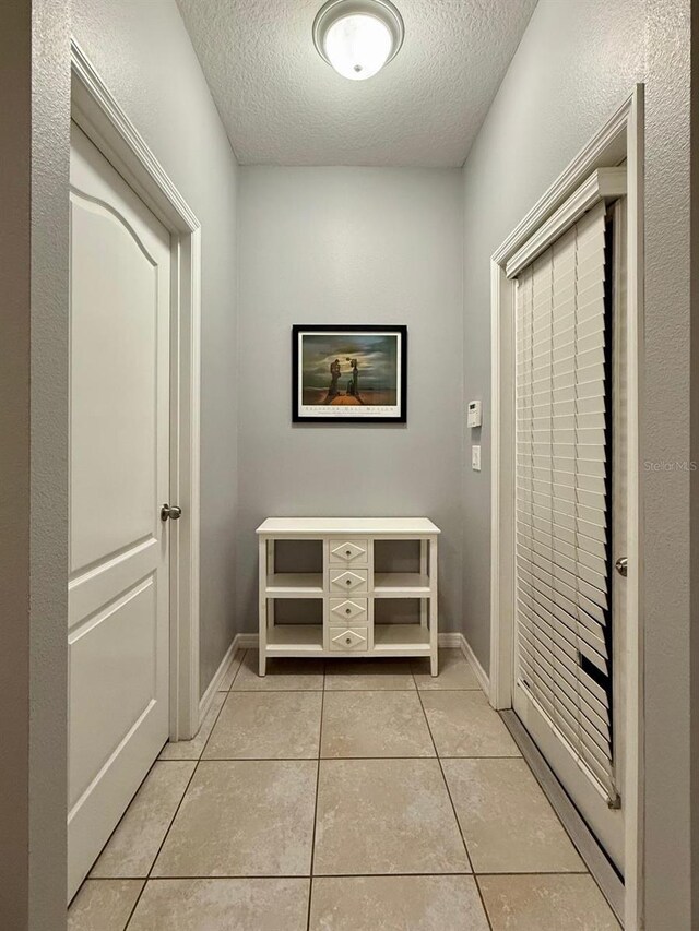 hall featuring light tile patterned floors, a textured ceiling, and baseboards