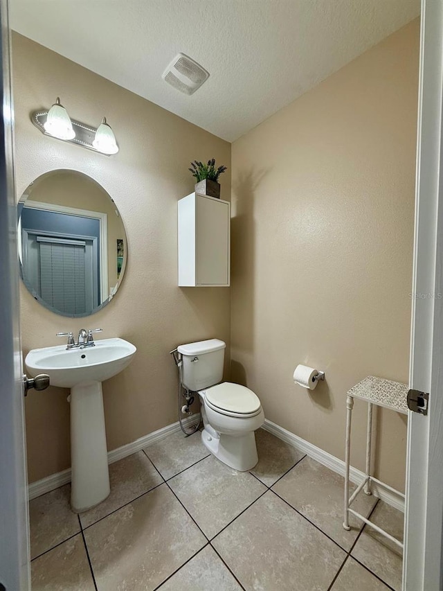 bathroom featuring baseboards, a textured ceiling, toilet, and tile patterned floors