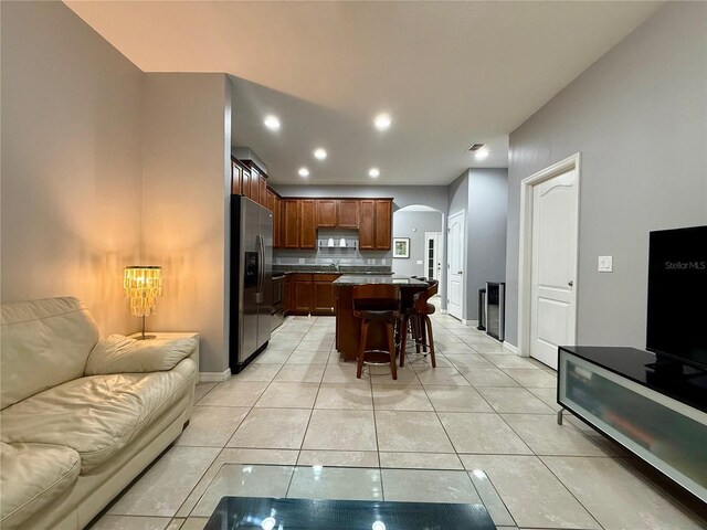 kitchen featuring light tile patterned floors, arched walkways, a breakfast bar area, open floor plan, and stainless steel refrigerator with ice dispenser