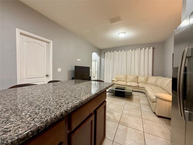 living area with arched walkways, light tile patterned floors, a textured ceiling, and visible vents