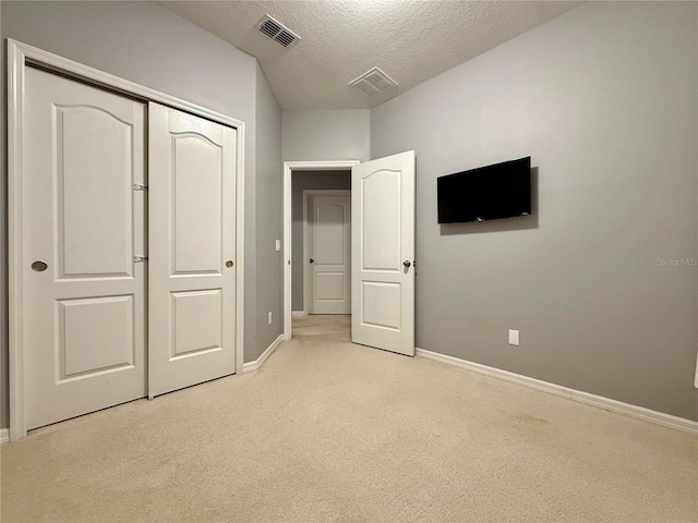 unfurnished bedroom with a textured ceiling, light colored carpet, visible vents, baseboards, and a closet