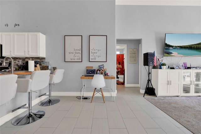 kitchen featuring a towering ceiling, baseboards, white cabinetry, and backsplash