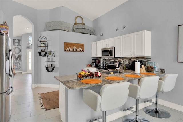 kitchen with stainless steel appliances, tasteful backsplash, white cabinetry, a peninsula, and a kitchen bar