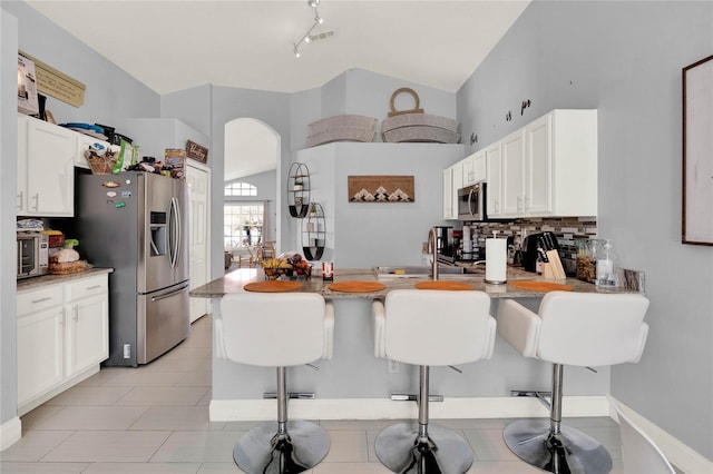 kitchen with tasteful backsplash, arched walkways, appliances with stainless steel finishes, a breakfast bar, and a sink