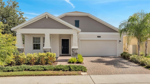 view of front of home with an attached garage, stone siding, decorative driveway, and stucco siding