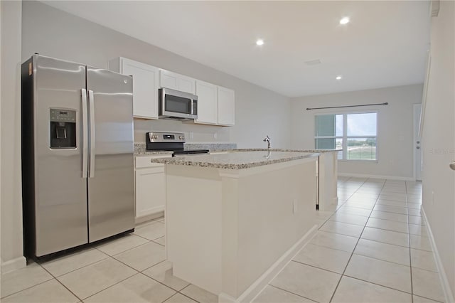 kitchen featuring light tile patterned floors, appliances with stainless steel finishes, a center island with sink, and white cabinetry