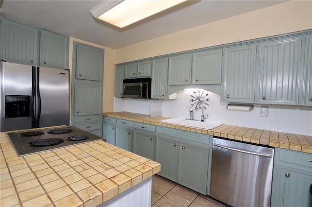 kitchen with stainless steel appliances, tile counters, a sink, and light tile patterned floors