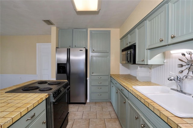 kitchen featuring tile countertops, stainless steel appliances, visible vents, wainscoting, and a sink