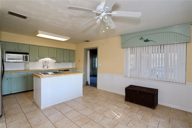 kitchen featuring tile countertops, stainless steel microwave, visible vents, wainscoting, and green cabinetry