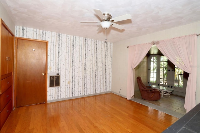 unfurnished room featuring a ceiling fan, wood finished floors, baseboards, and wallpapered walls