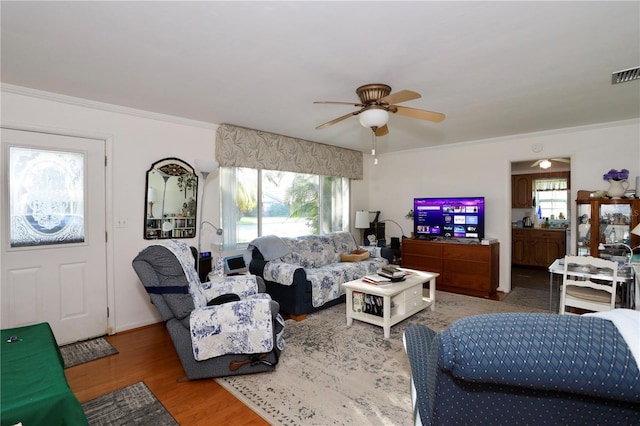 living area featuring ceiling fan, crown molding, visible vents, and wood finished floors