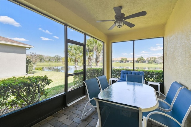 sunroom with a ceiling fan and a water view