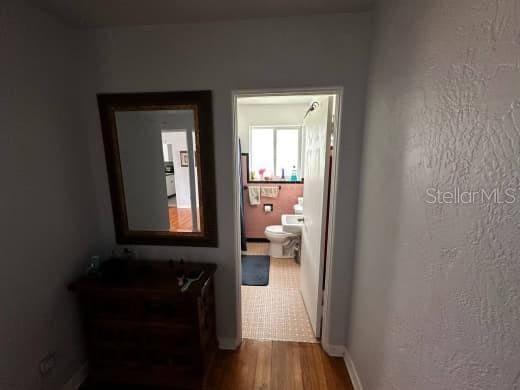 hallway with a textured wall, baseboards, and wood finished floors