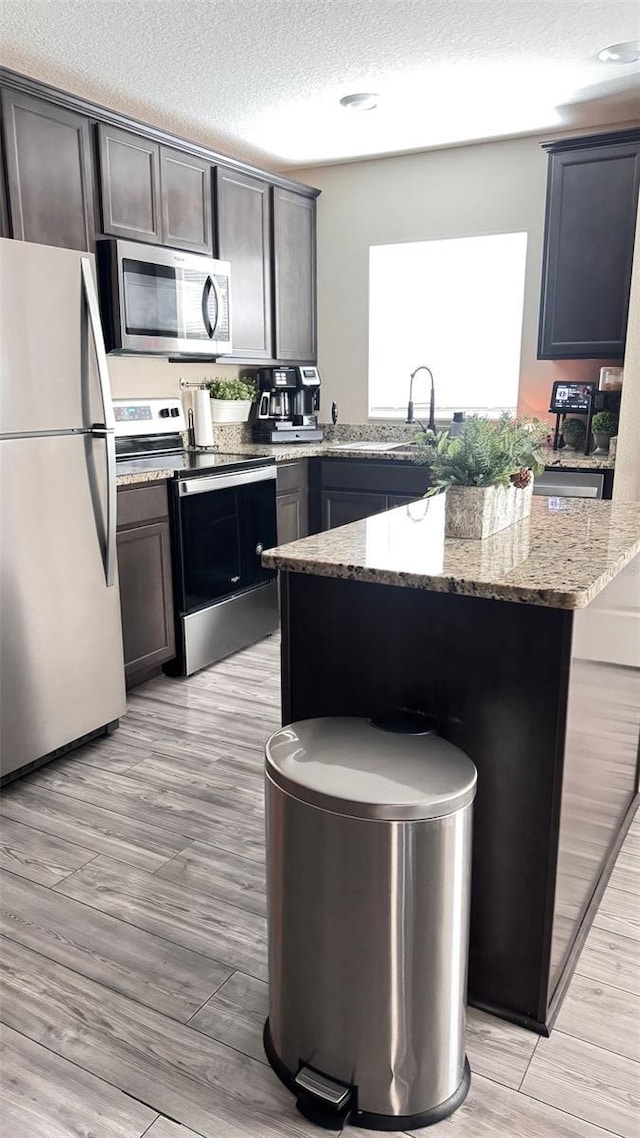 kitchen with a textured ceiling, stainless steel appliances, light stone counters, and light wood-type flooring