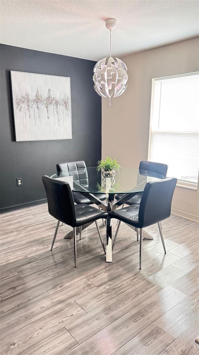 dining space with light wood-style floors, baseboards, and a textured ceiling