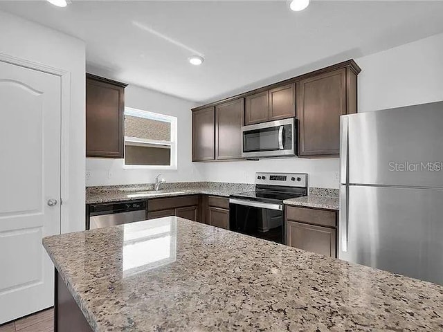 kitchen with a sink, dark brown cabinetry, appliances with stainless steel finishes, and light stone counters