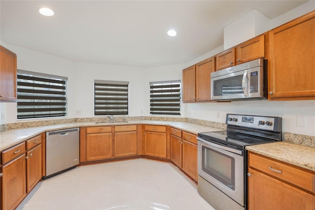 kitchen featuring appliances with stainless steel finishes, brown cabinetry, a sink, and recessed lighting