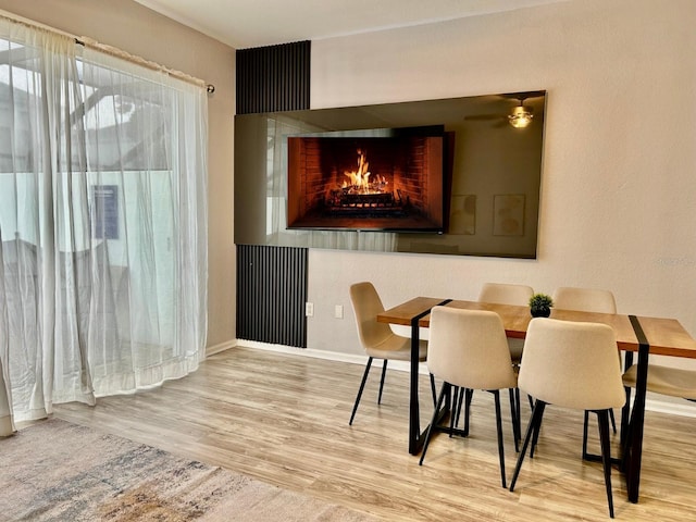 dining area featuring a lit fireplace, baseboards, and wood finished floors