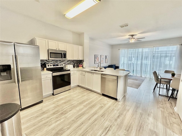 kitchen with stainless steel appliances, tasteful backsplash, visible vents, a sink, and light wood-type flooring