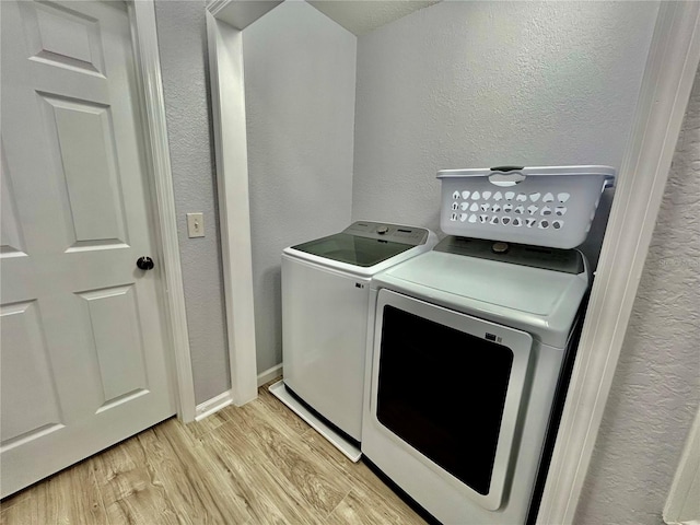 laundry area featuring laundry area, baseboards, a textured wall, independent washer and dryer, and light wood-style floors