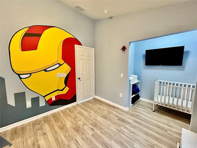 bedroom with a nursery area, visible vents, baseboards, and wood finished floors