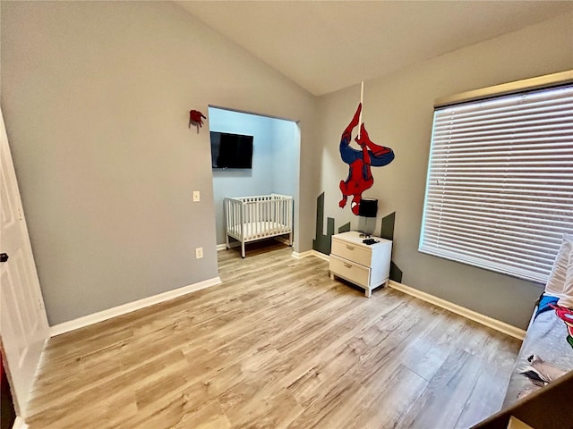 bedroom featuring a nursery area, light wood-style flooring, baseboards, and vaulted ceiling