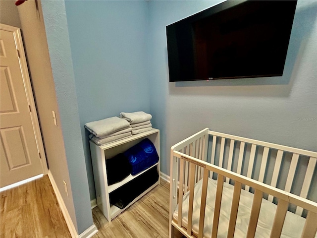 bedroom featuring a nursery area, baseboards, and wood finished floors