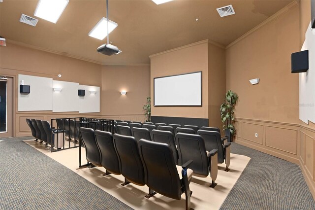 carpeted cinema room with crown molding, visible vents, and a decorative wall