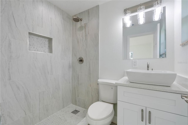 full bathroom featuring a tile shower, vanity, and toilet