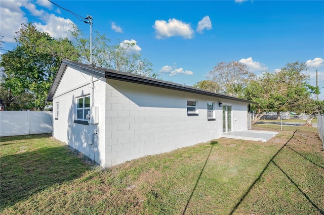 rear view of house featuring fence, concrete block siding, and a yard